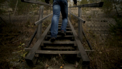 Man man going up stairs. Footage. The old wooden steps on a hill rising on either side grass. Wood stairs up a grass hill