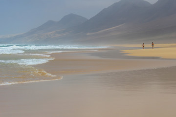 Romantic walk on a edge of ocean surf on magnificent Cofete beach in secluded part of Fuerteventura, Canary Islands, Spain