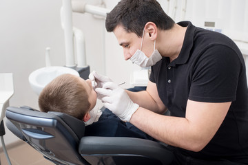 Pediatric dentist examining teeth of boy patient in dental clinic using dental tools - probe and mirror. Dentistry