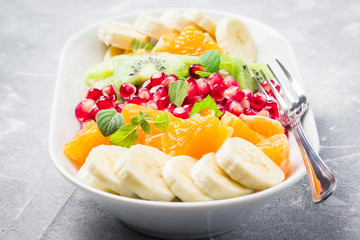 Colorful fruit salad with mint lemon dressing on stone background. Selective focus, close up. 