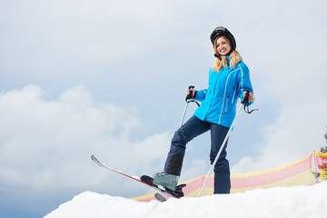 Sporty girl skier wearing blue ski suit and black helmet, smiling to the camera, enjoying skiing in...