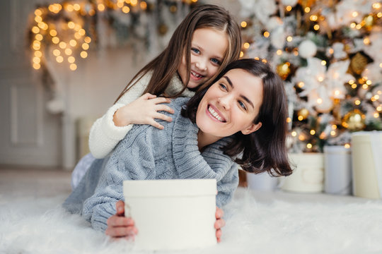 Happy female model with short dark hair and her adorabe small girl have fun together, celebrate Christmas, exchange presents, have smiling expressions, have joy. Friendly family with presents