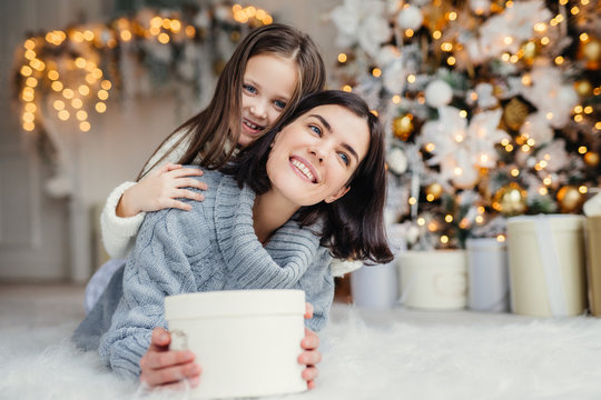 Portrait of happy mother and daughter spend free time together, embrace each other, have pleasant smiles, hold wrapped present boxes, celebrate New Year or Christmas together. Holidays concept