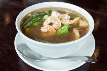 Spicy vegetable and prawn soup in bowl on wooden table