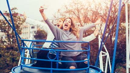 Obraz na płótnie Canvas Two girls taking selfie while having fun in amusement park