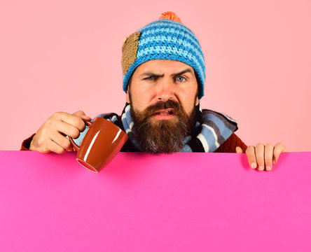 Man in warm hat holds brown cup on pink background