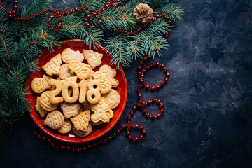 Christmas cookies in a red plate on a black background with spruce branches and Christmas decorations