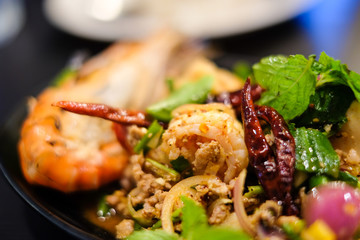 Big shrimps and squids and spicy minced pork mixed together with various herbs and vegetables including dried chilli served on black plate, for thai food background or texture.