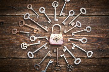 Vintage rusty padlock surrounded by old keys on a weathered wooden background