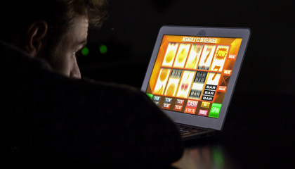 Gambling addicted man with glasses in front of online casino slot machine on laptop computer at...