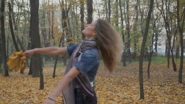 Happy woman walks in autumn park with bouquet of leaves