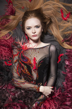 Romantic look. Interesting ginger model surrounded with feathers