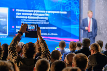 Man takes a picture of the presentation at the conference hall using smartphone