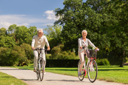 happy senior couple riding bicycles at summer park