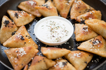 Close-up of meat samosas topped with sesame seeds and served with sauce, selective focus