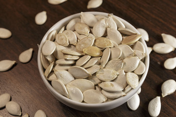 Vegan food. Raw pumpkin seeds for roasting in a white dish. Wooden background.