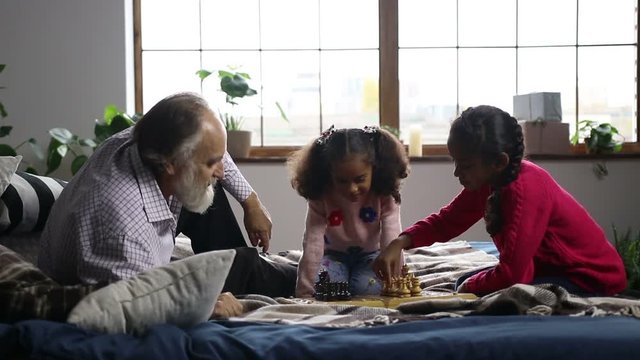 Elderly man playing chess with cute granddaughter