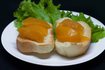 Close up view of two toast with delicious peach jam with a leaf of salad in plate isolated on dark background