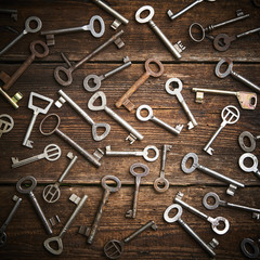 Many different keys on brown grunge wooden background.
