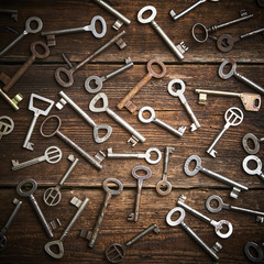 Many different keys on brown grunge wooden background.
