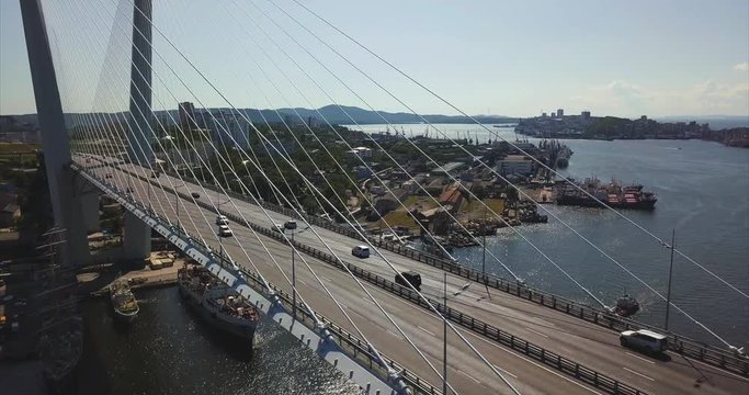 Ascending aerial view of the Golden Bridge (built in 2012) and cars driving along it. It's cable-stayed bridge across the Zolotoy Rog harbour. Vladivostok is on the background. Russia