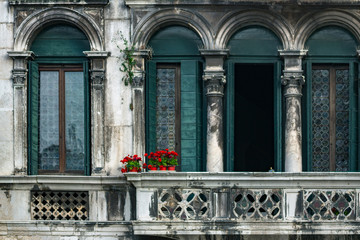 Fototapeta na wymiar Ancient balcony in Venice, Italy. Venetian architecture. Red flowers in pots against background of a vintage building in Venice, Italy. Venetian balcony. Red flowers on an old balcony without people.