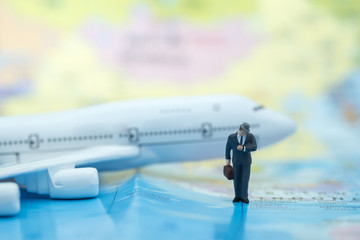 Business travel and time concept. Businessman miniature figure looking to wriest watch and standing on world map with airplane as background.