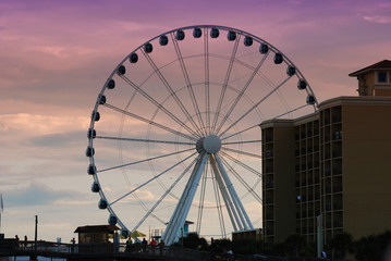 A large ferris wheel in down Myrtle Beach, South Carolina as the sun sets against a purple sky.
