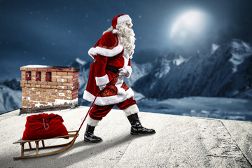 Crazy Santa Claus on a sledge. He's on the roof of the house. Beautiful December night with a big moon in the sky and a view of the mountains full of snow.