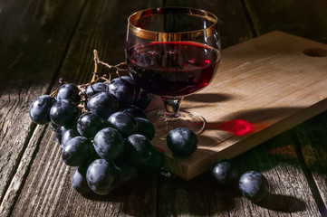 Dark grapes and red wine in a glass. Still life in the hard light on a rustic background.
