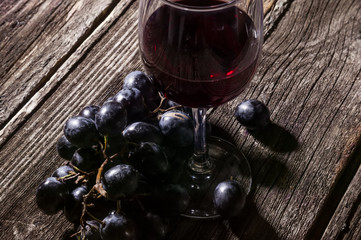 Dark grapes and red wine in a glass. Still life in the hard light on a rustic background.