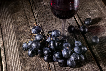 Dark grapes and red wine in a glass. Still life in the hard light on a rustic background.