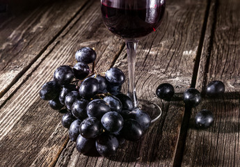 Dark grapes and red wine in a glass. Still life in the hard light on a rustic background.