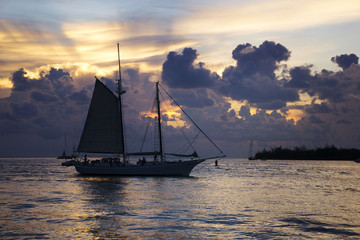 A sailboat in the ocean in front of purple clouds after sunset in Key West, Florida.
