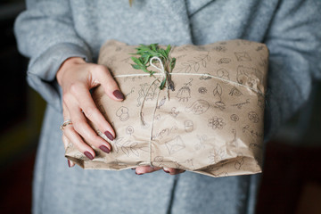 Obraz premium Hands in a gray coat hold a gift, New Year, preparing a gift, packaged in a rustic style, rosemary 