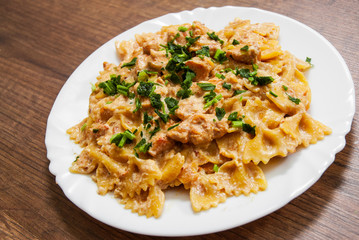 Sliced fried chicken fillet in a creamy sauce. with farfalle pasta. in plate on a wooden background