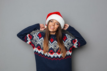 Happy young woman dressed in sweater wearing christmas hat