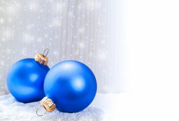 Two christmas toys blue balls are lying in snow on wooden white background and copy space.