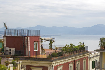 Dettaglio di un terrazzo su un palazzo rosso che affaccia sul mare del golfo di Napoli. Sul grande balcone ci sta un gazebo e delle piccole piante