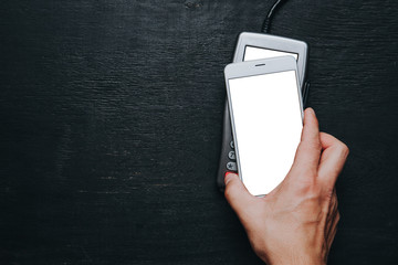 Top view of person using contactless payment with smartphone. Clear white mockup screen template of phone and pos terminal on dark wooden desk with side copy space
