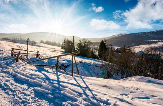 broken fence on a snowy slope in rural are. lovely winter landscape with bright sun over the mountain ridge
