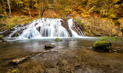 Fototapeta na wymiar Autumn waterfall in a wood. Picturesque wood in warm colors.
