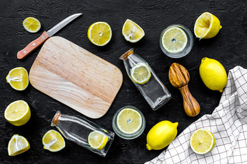 Make lemonade at home. Lemons, juicer, glass and bottle for beverage, knife, cutting board on black background top view