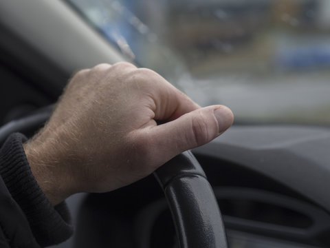 close up man hand holding streering wheel view from inside of th car defocused background