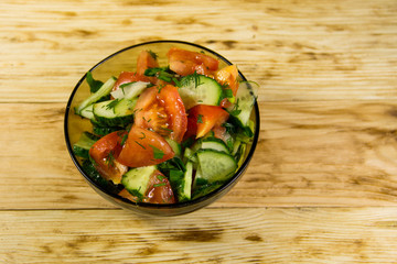 Fresh salad with tomato, cucumber, onion, parsley and dill in glass bowl on wooden table