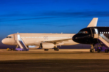 Obraz premium White and black passenger airplanes on the apron of the airport at dusk
