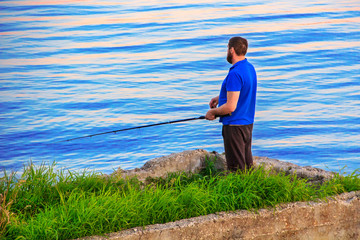 Fototapeta na wymiar A man stands on the river bank with a fishing rod.