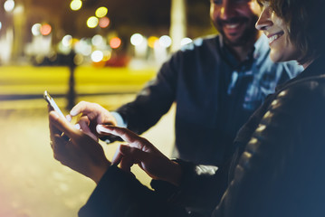 People together pointing finger on screen smartphone on background bokeh light in night atmospheric city, group adult hipsters friends using in hands modern mobile phone wi-fi internet