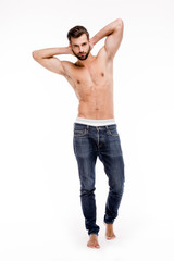 Fototapeta premium Perfect stubble man. Full length of handsome young man in jeans looking at camera and keeping hands behind head while standing against white background.