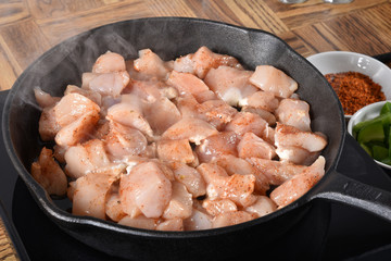 Diced chicken breasts cooking in a cast iron skillet